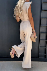 Back view of a woman in a round neck cap sleeve jumpsuit in neutral color, highlighting silhouette and stylish design.