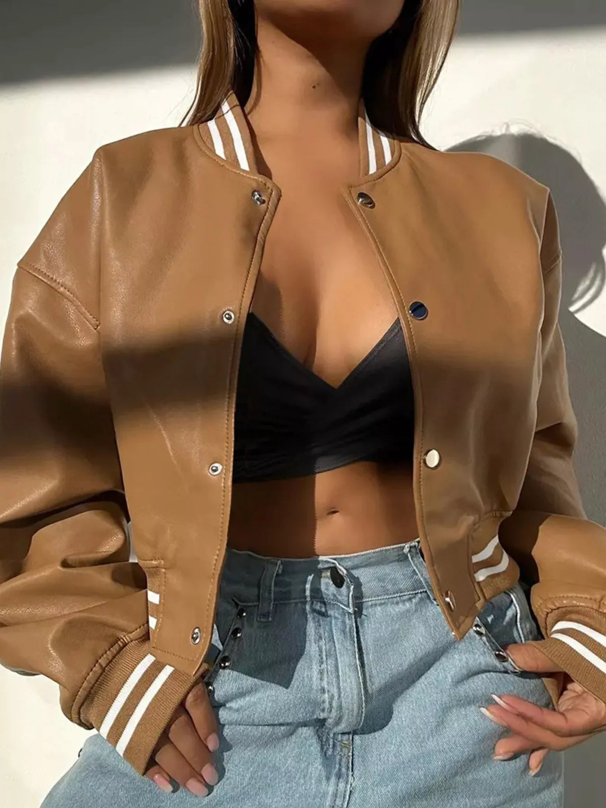 Brown snap down long sleeve jacket with white trim, styled with a black top and high-waisted jeans.