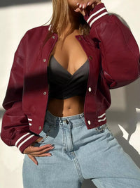 Model wearing a burgundy snap down long sleeve jacket with white stripes, styled casually with high-waisted jeans.