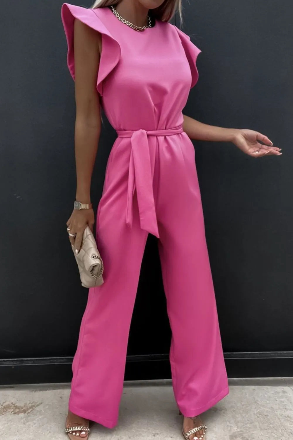 Pink round neck cap sleeve jumpsuit with a tied belt and ruffle details, perfect for a stylish look.