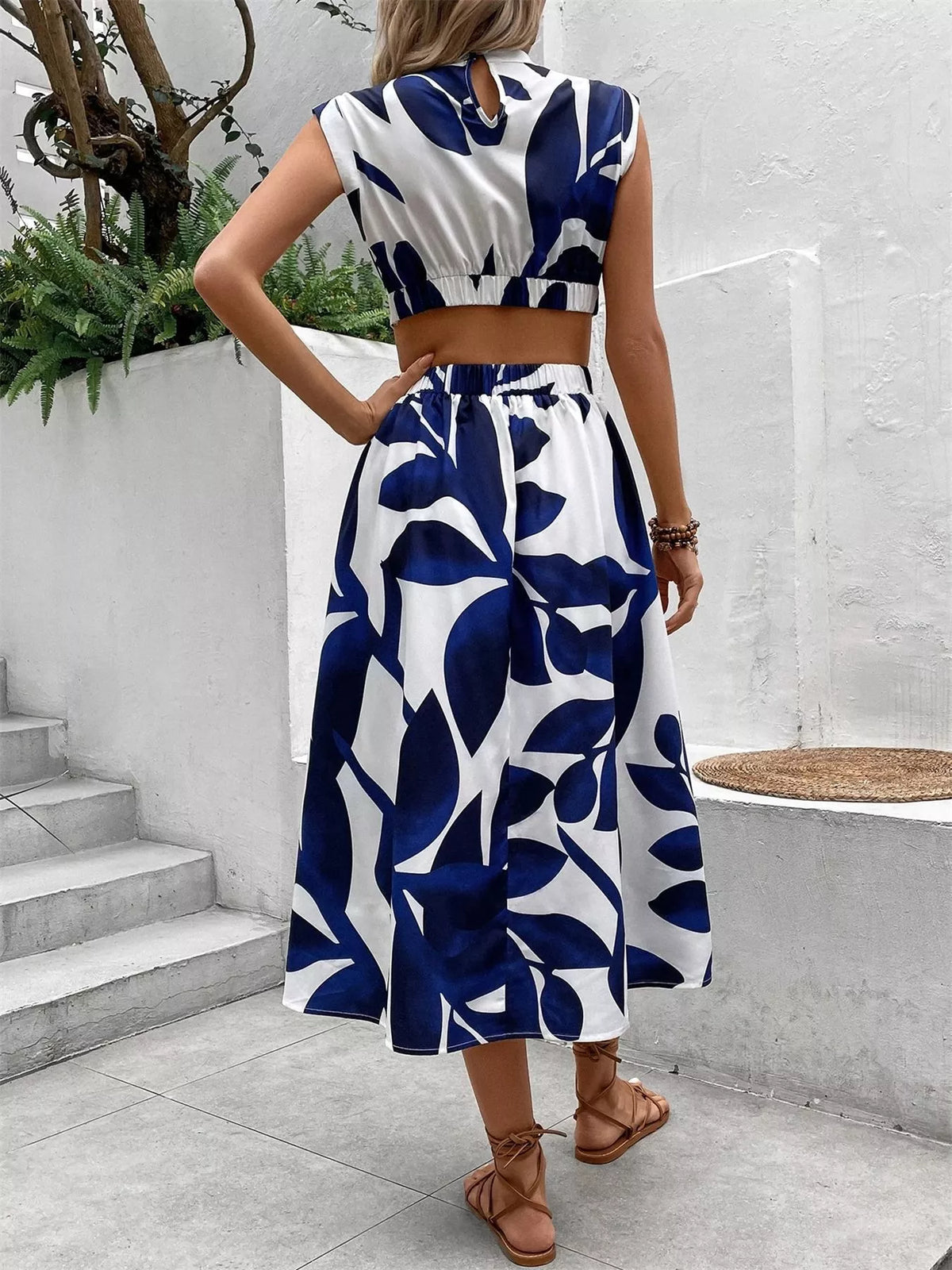 Woman wearing a back view of a cutout printed sleeveless dress with a leaf pattern in navy and white.