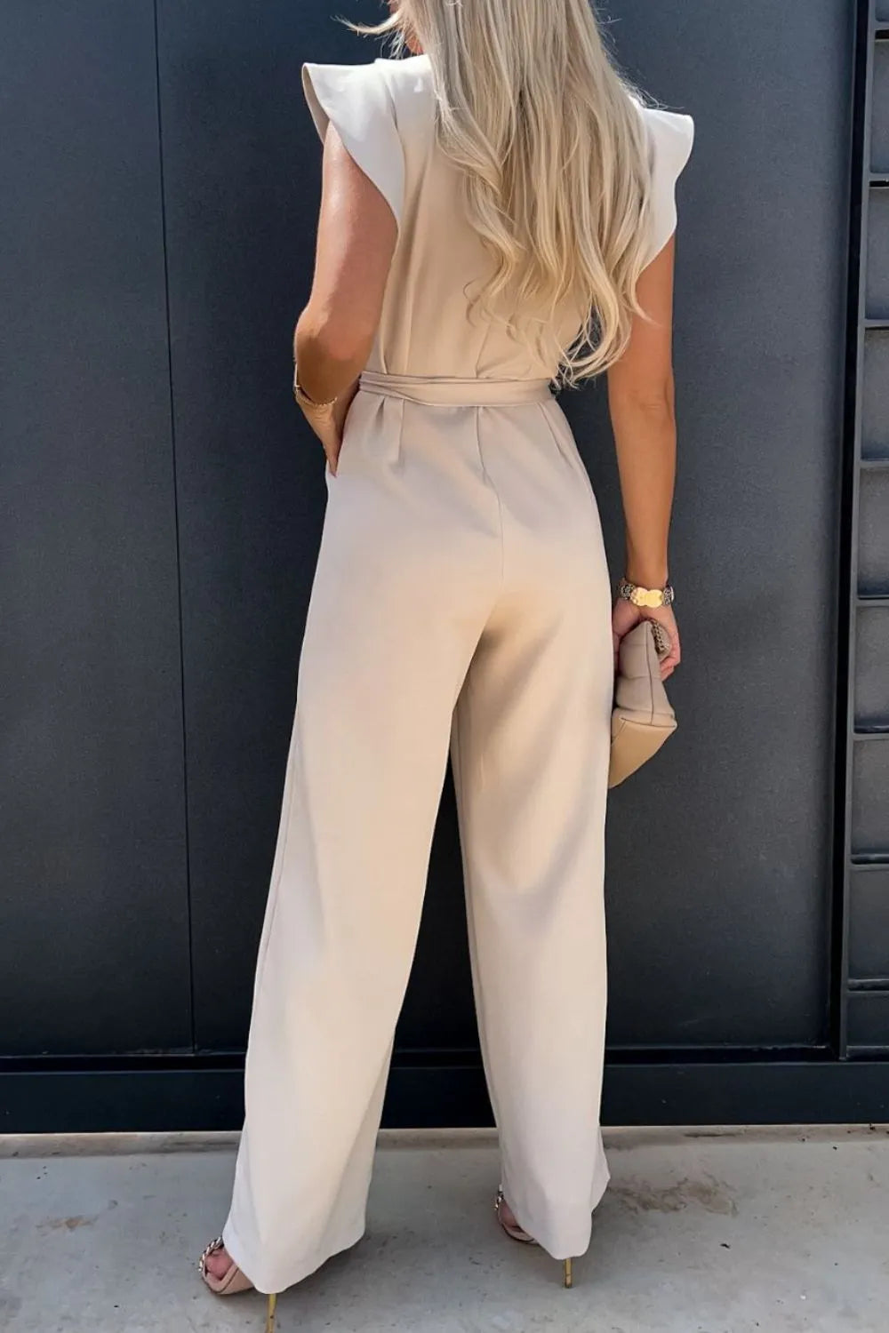 Back view of a woman wearing a beige round neck cap sleeve jumpsuit, showcasing its stylish design and flowing silhouette.