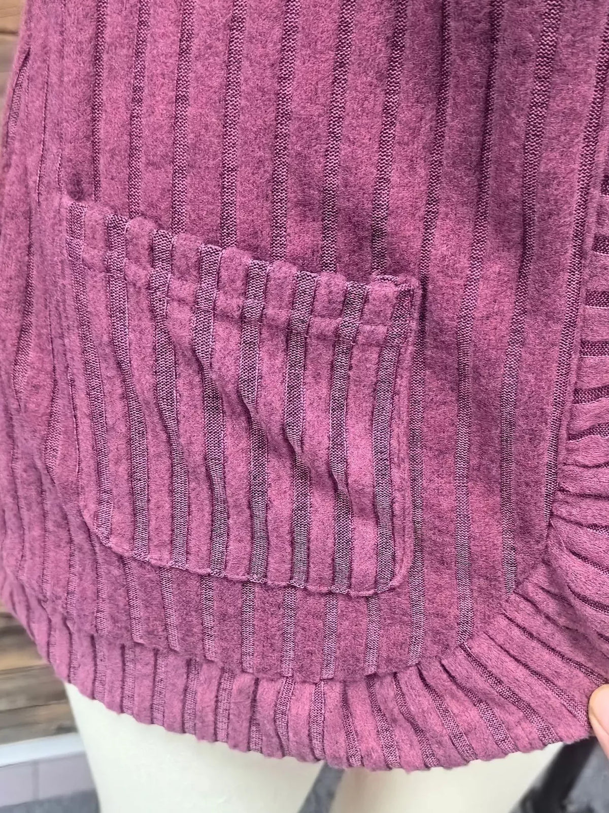 Close-up of open front ribbed knit cardigan in mauve with pocket detail and textured fabric.