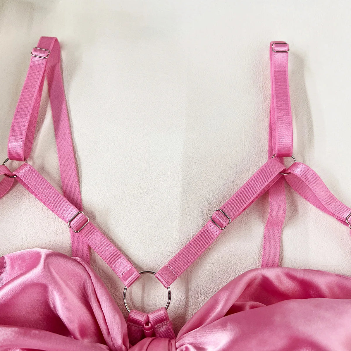 Close-up of pink satin lingerie straps featuring adjustable buckles and a circular ring, highlighting elegance.