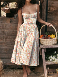 Model wearing a floral print cami dress with a sweetheart neckline, standing beside a basket of fruits.